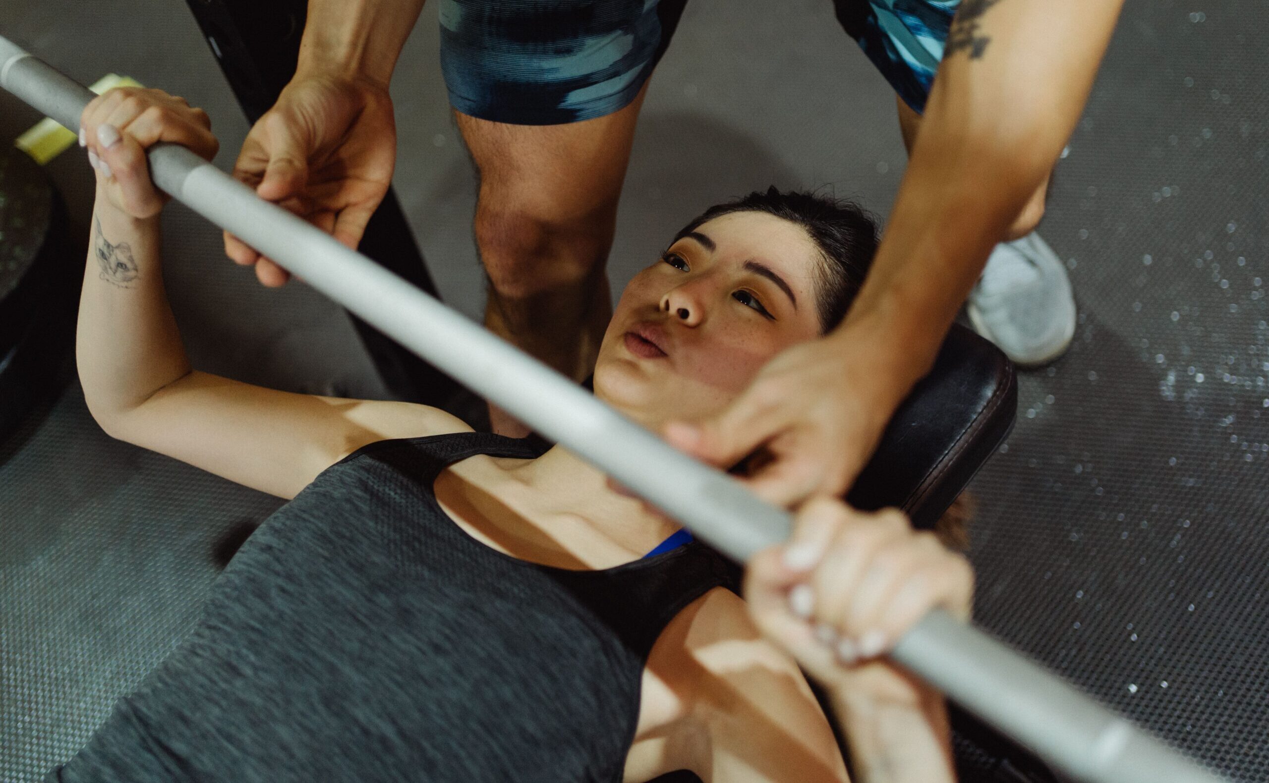 Woman performing bench press exercise with guidance in a gym setting.